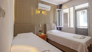A hotel room with two beds, a wooden slat wall, an air conditioning unit, and a window with a view. - GÜL PENSİON (Fethiye)