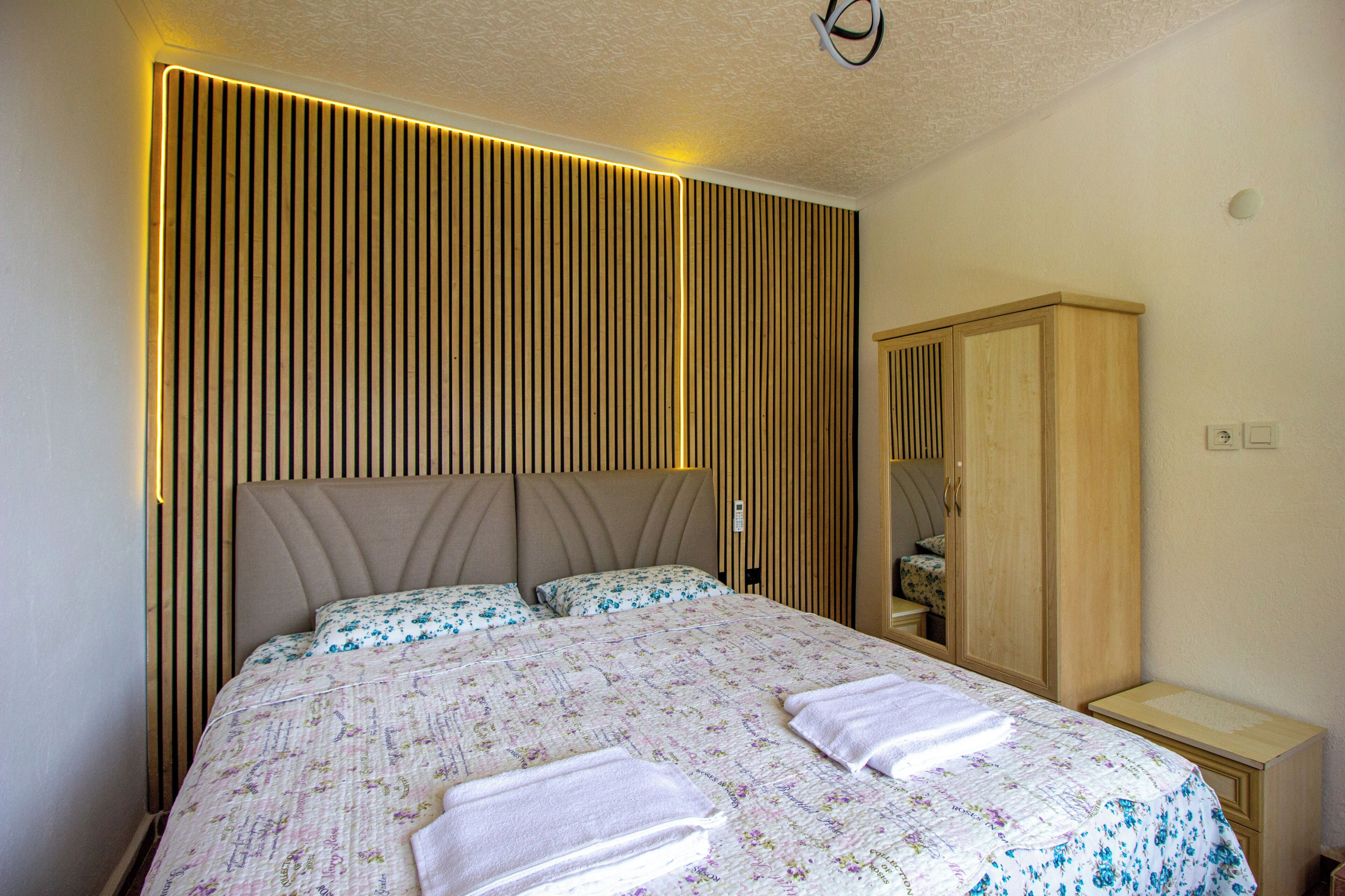 A bedroom with a large bed, a wooden wardrobe, and a wall with vertical slats.