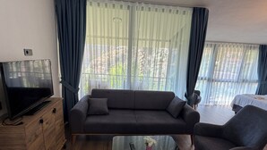 Un soggiorno con divano, tavolino, televisore e vista panoramica attraverso ampie finestre.
