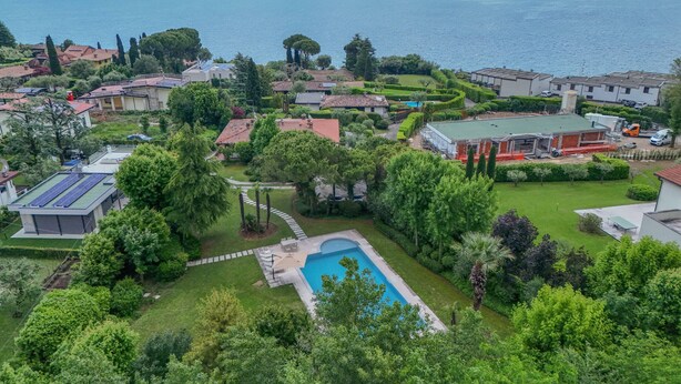 A residential area with a swimming pool surrounded by lush greenery and houses with red-tiled roofs. - Villa Maria with private pool (Moniga del Garda)