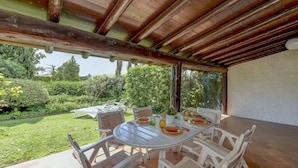 An outdoor patio with a round table and white chairs, surrounded by a garden and a wooden pergola. - Villa Maria with private pool (Moniga del Garda)