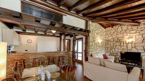 A spacious living area with a glass dining table, wicker chairs, a white sofa, and a stone wall. - Villa Maria with private pool (Moniga del Garda)