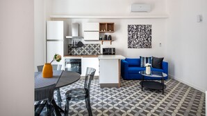 A modern kitchen with white cabinets, a microwave, and a coffee machine. There is a dining area with a table and chairs, and a blue sofa in the living area. - Ci Capo 2 by Wonderful Italy (Palermo)