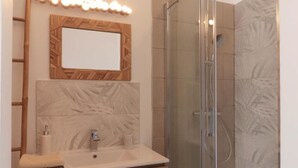 Un baño con cabina de ducha de vidrio, tocador de madera con espejo y una toalla sobre la encimera.