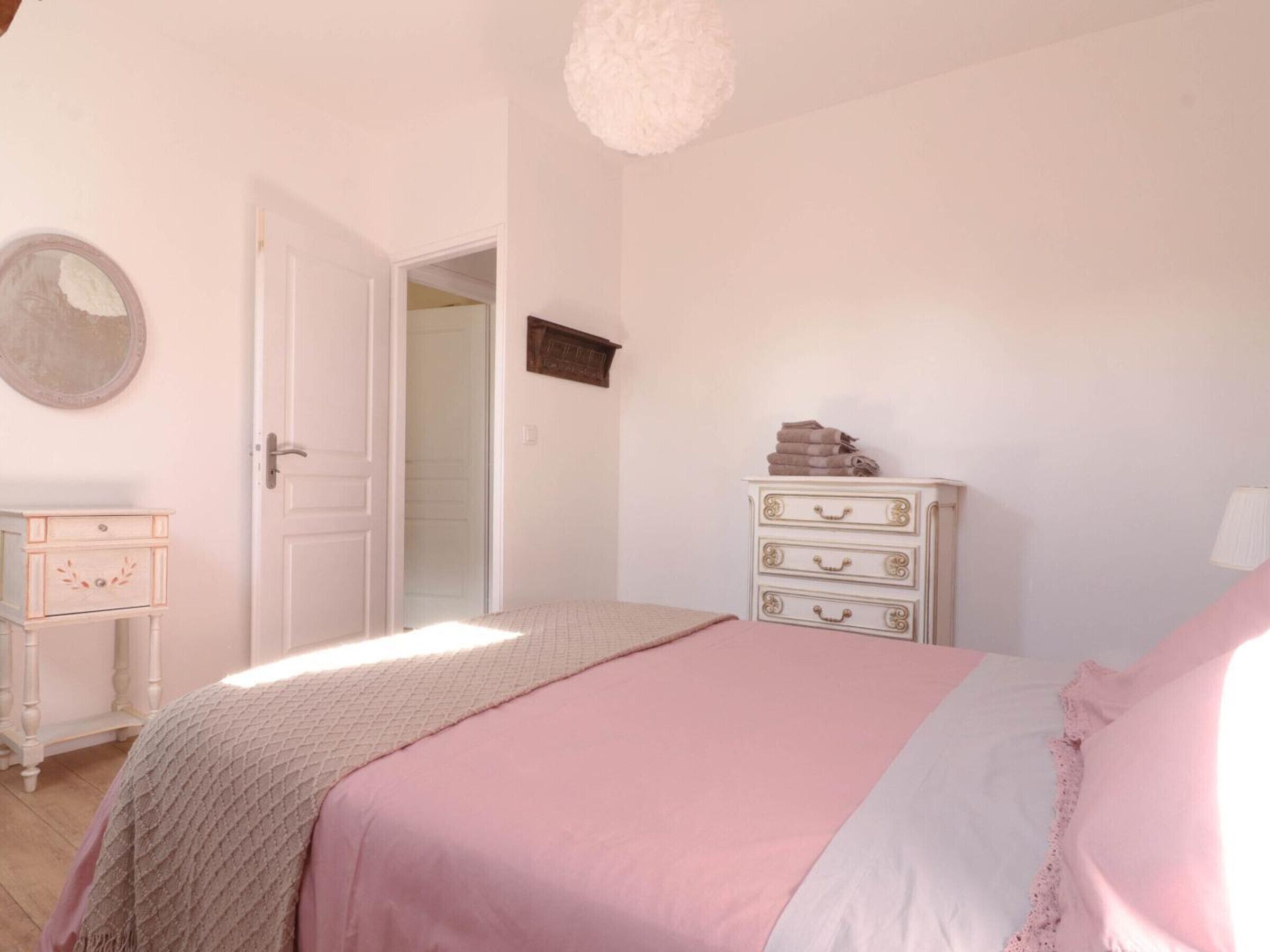 Een slaapkamer met een bed, een kapstok en een deur naar een andere kamer.