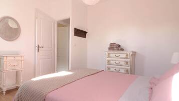 Een slaapkamer met een bed, een kapstok en een deur naar een andere kamer.