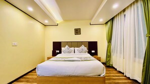 Une chambre d’hôtel avec un lit en bois, une table de chevet, une prise électrique au mur et une fenêtre avec des rideaux verts.