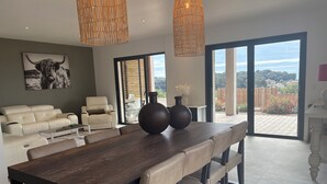A modern dining area with a wooden table and chairs, a sofa, and a large window with a view of the outdoors. - Villa with swimming pool, very quiet, near Cannes/Juans les pins (Vallauris)