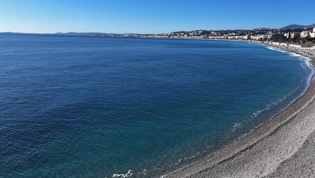 A coastal beach with clear blue waters, a pebbly shore, and a cityscape in the background. - Villa with swimming pool, very quiet, near Cannes/Juans les pins (Vallauris)