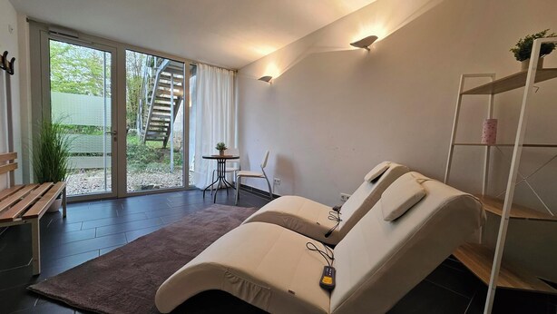 A modern room with a massage table, a small table with chairs, and a view of a staircase and greenery outside. - Vacation in the vacation apartment Morgenröte with sauna and terrace centrally located in Mirow (Mirow)