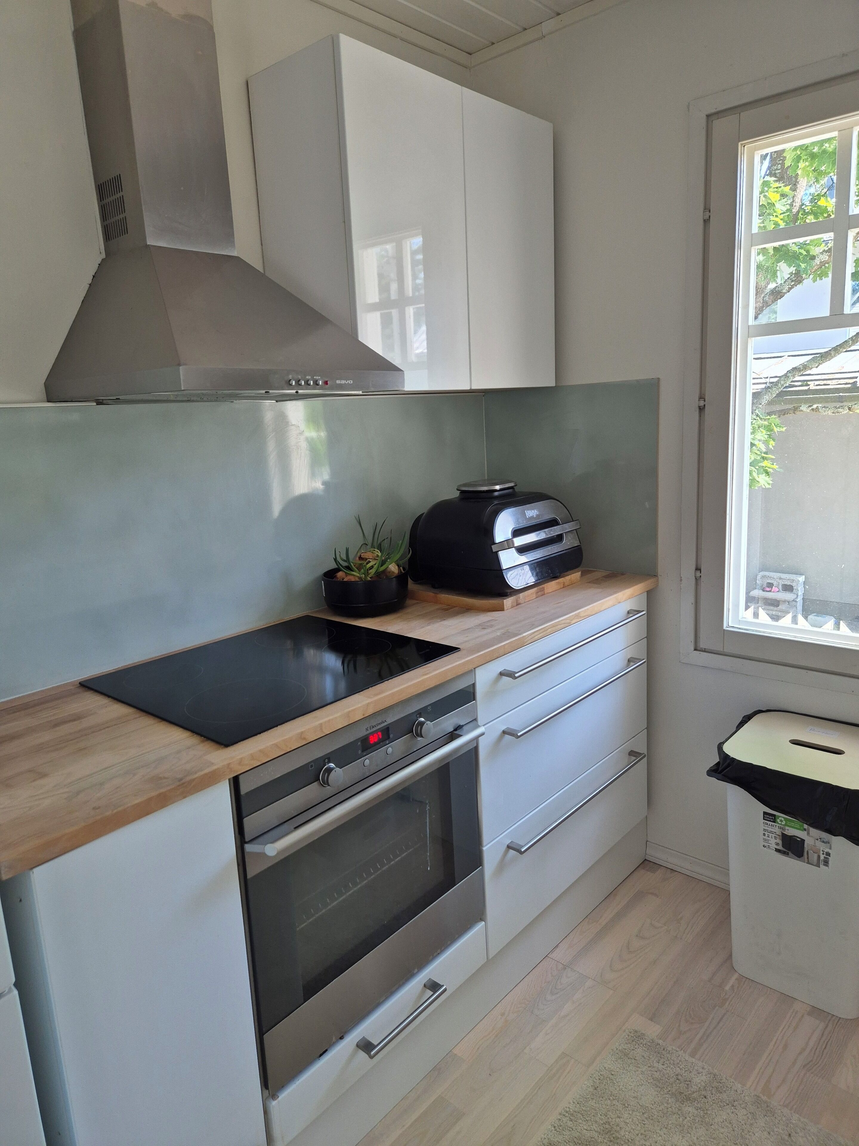 A modern kitchen with a built-in oven, a stainless steel range hood, and a window with a view of the outside.