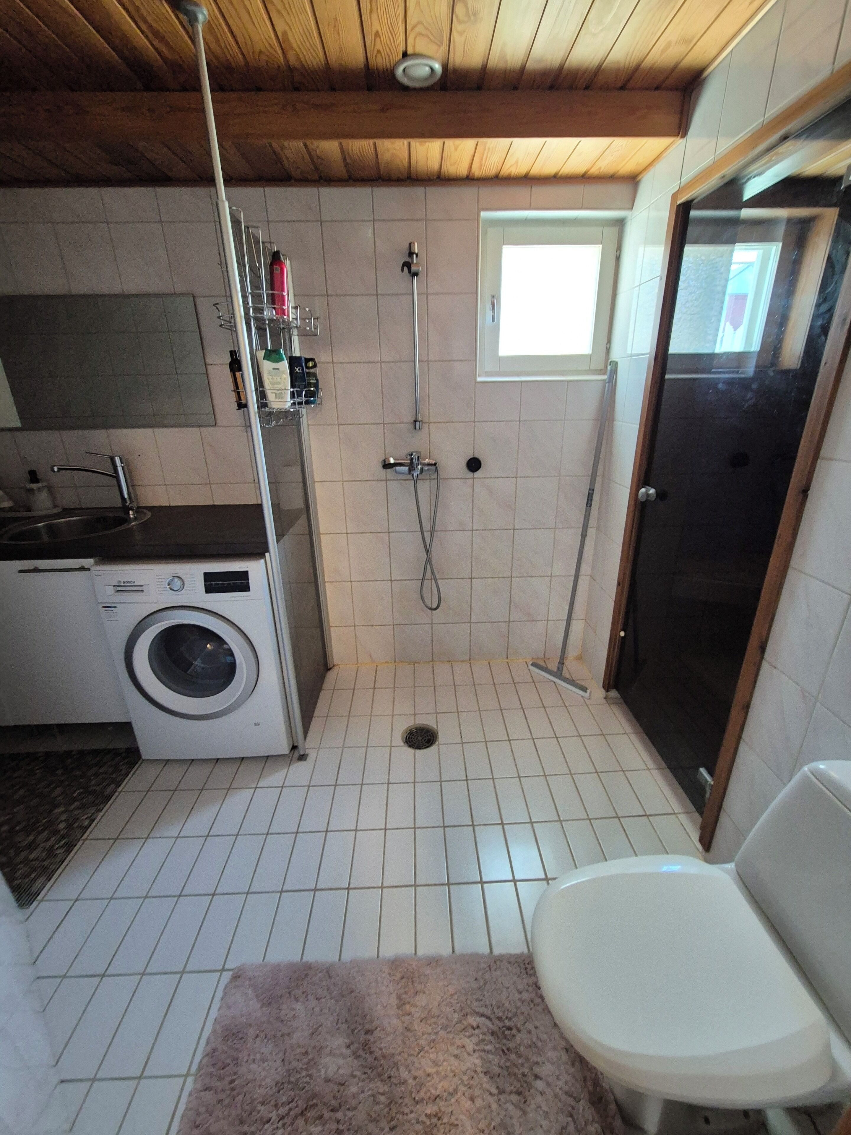 Une petite salle de bain comprenant une douche, des toilettes et un lave-linge.