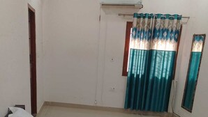 A bedroom with a bed, a window with curtains, an air conditioning unit, and a door. - Ashiyana Upvan Homestay (Lucknow)