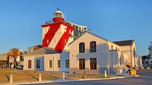 Un faro con torre a rayas rojas y blancas, junto a un edificio blanco con varias ventanas y techo plano.