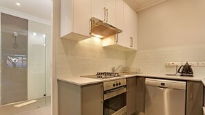 Cocina moderna con electrodomésticos de acero inoxidable, lavavajillas y cabina de ducha con mampara de vidrio.