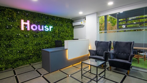 A reception area with a green wall, a reception desk, two chairs, and a glass table. - Housr 43 Gachibowli Near DLF Cybercity (Hyderabad)
