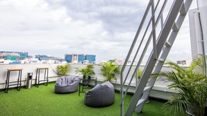 A rooftop terrace with green artificial grass, two bean bags, a small table with a potted plant, and a view of the city skyline. - Housr 43 Gachibowli Near DLF Cybercity (Hyderabad)