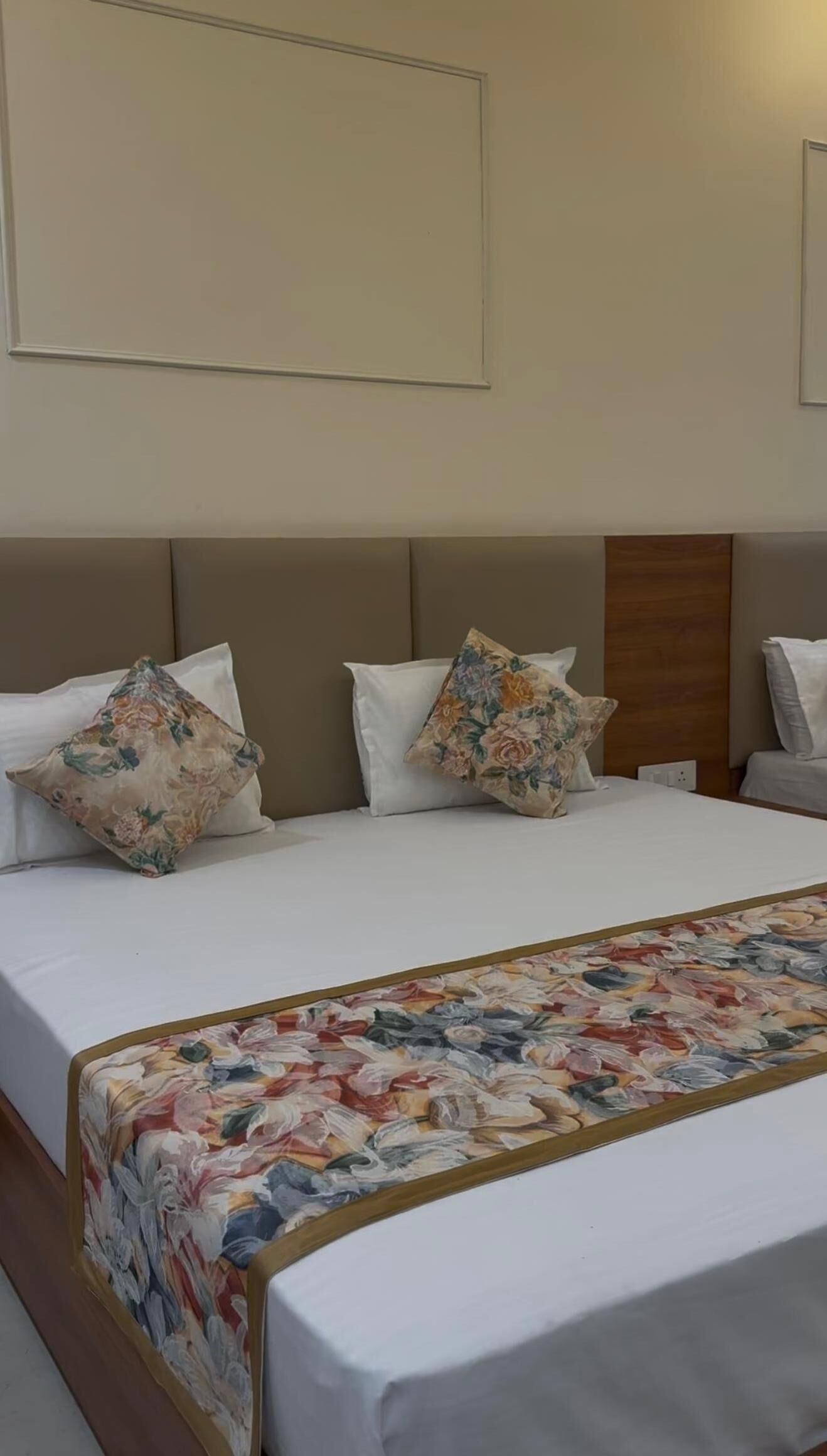 A hotel room with a large bed, two pillows, a floral bedspread, and a wooden headboard.