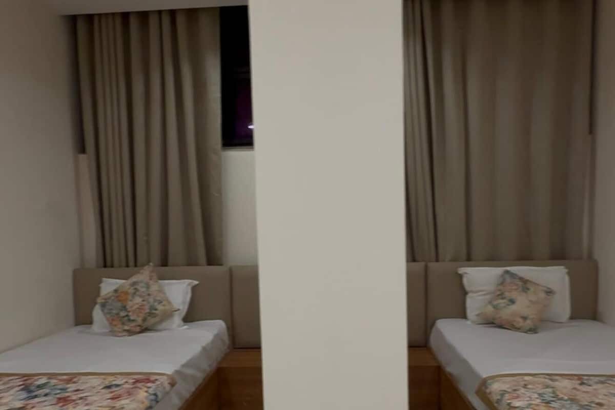 A modern hotel room with two single beds, a large window with curtains, and a ceiling fan.