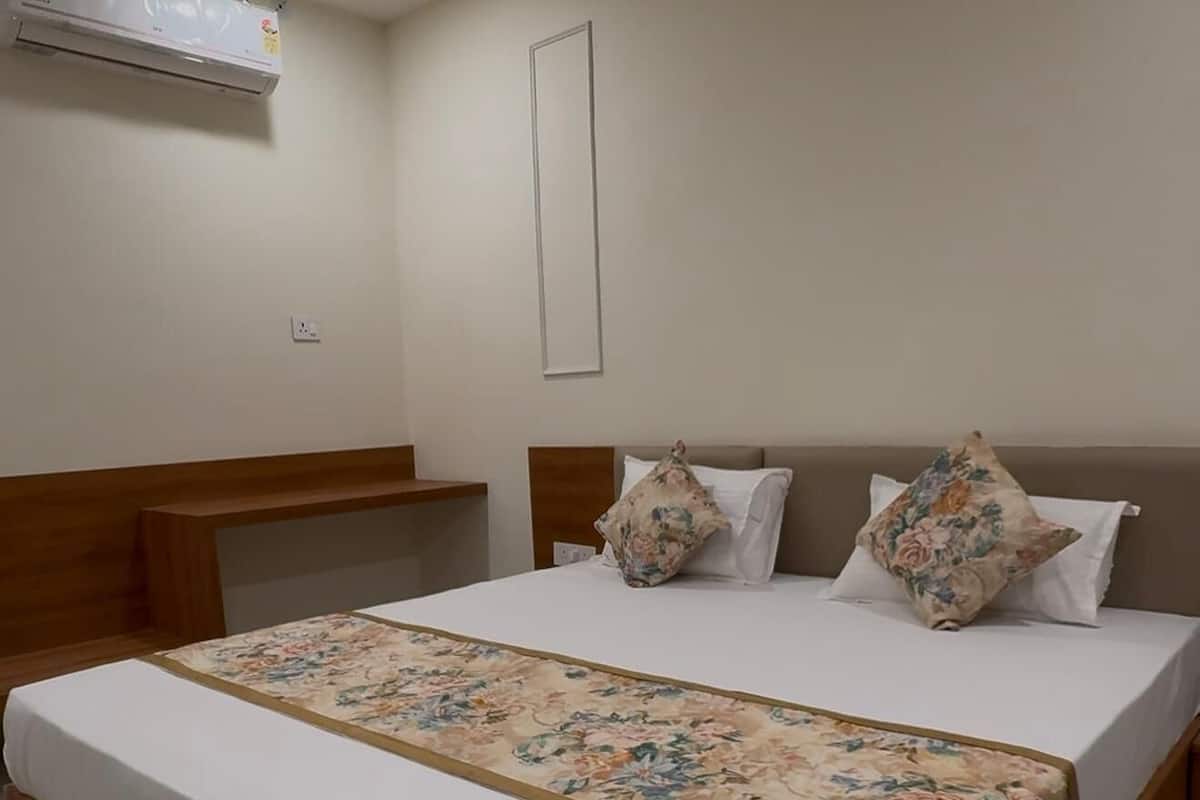 A hotel room with a large bed, wooden headboard, white bedding, and a floral bedspread.