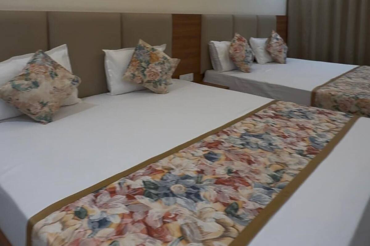 A hotel room with two beds, each with floral-patterned bedding and matching pillows. The room has a neutral color scheme with beige walls and a wooden headboard.