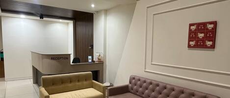 A reception area with a reception desk, two sofas, a wall-mounted artwork, and a tiled floor.