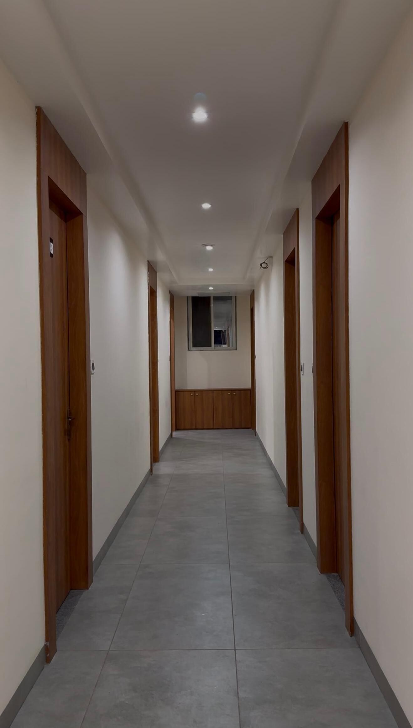 Um corredor comprido e estreito com portas de madeira em ambos os lados e piso de azulejos.