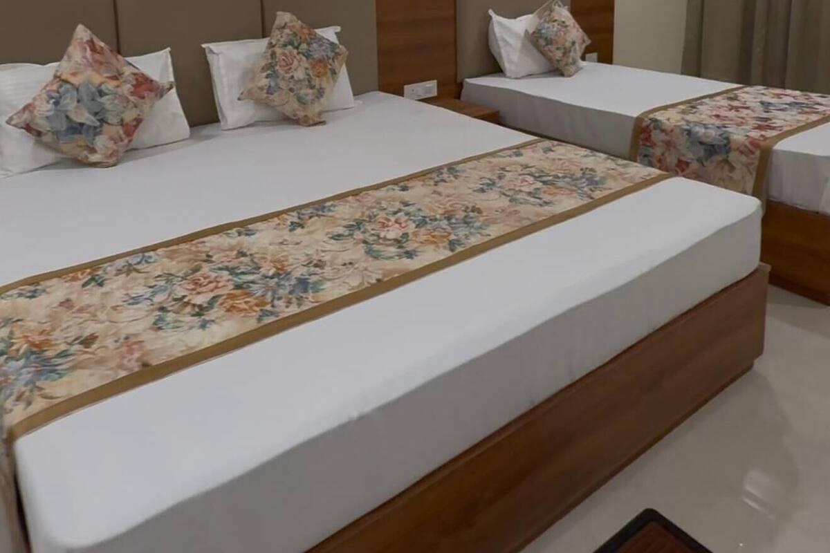 A hotel room with two single beds, a large bed, a ceiling fan, and an air conditioning unit.