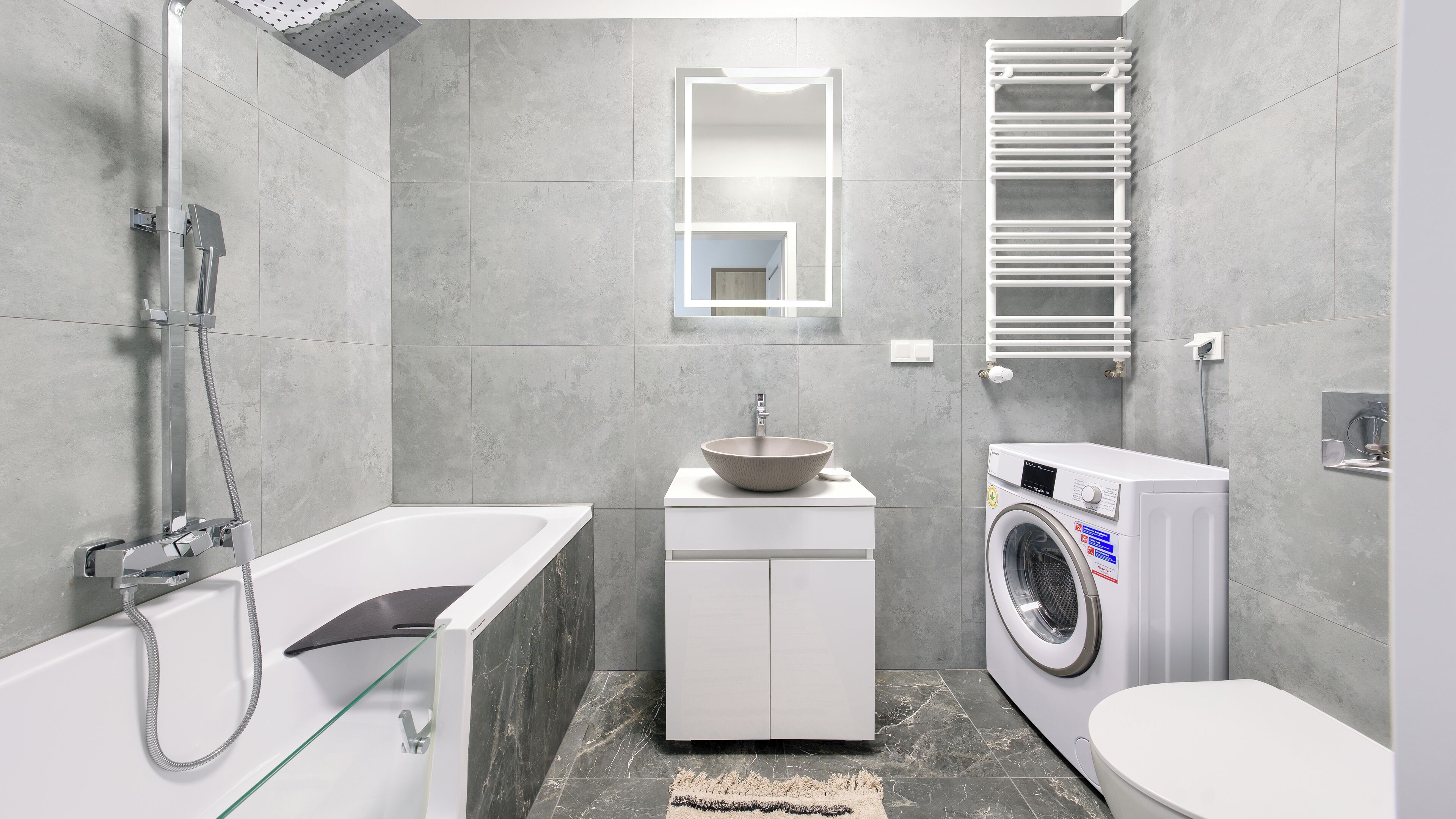 Ein modernes Badezimmer mit einer gläsernen Badewanne, einem Waschbecken mit Hohlbodenschale, einer eingebauten Waschmaschine und einem Handtuchhalter.