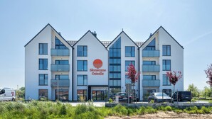 A modern building with a white facade and multiple balconies, featuring a logo with a red circle and the text "Stoneczne Osiedle". - Apartamenty Sun & Snow Słoneczne Osiedle (Ustronie Morskie)