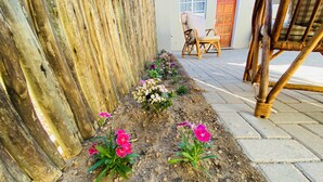 Een tuin met een houten omheining, een geplaveid pad en een rieten stoel.