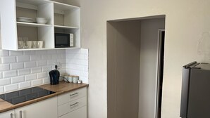 Een keuken met witte kastjes, een magnetron en een koffiezetapparaat op het aanrecht.
