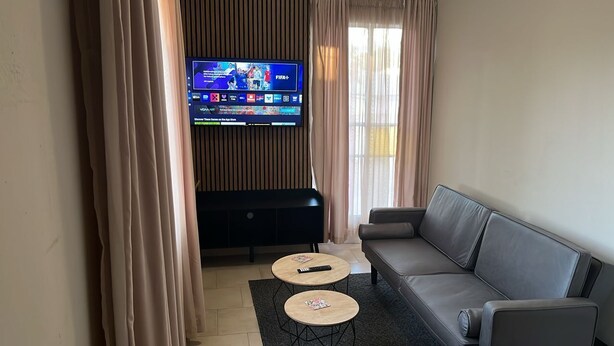 Een woonkamer met een flatscreen televisie aan de muur, een grijze bank, twee ronde salontafels en een zwarte tv-kast.