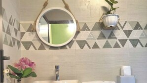 A bathroom with a white sink, a round mirror, a potted plant, and a geometric tile backsplash.