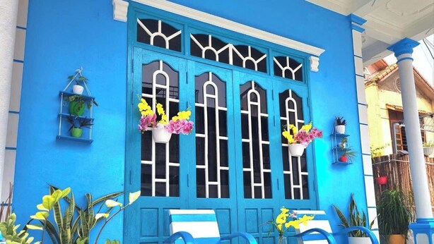 A blue building with large windows, outdoor seating, and potted plants.