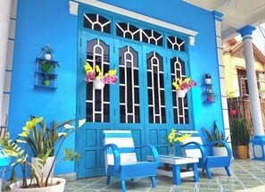 A blue building with large windows, outdoor seating, and potted plants.
