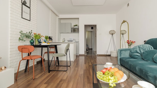 A modern living room with a teal sofa, a dining area with orange chairs, and a kitchen in the background. - ShortStayPoland Sielecka B183 (Warsaw)