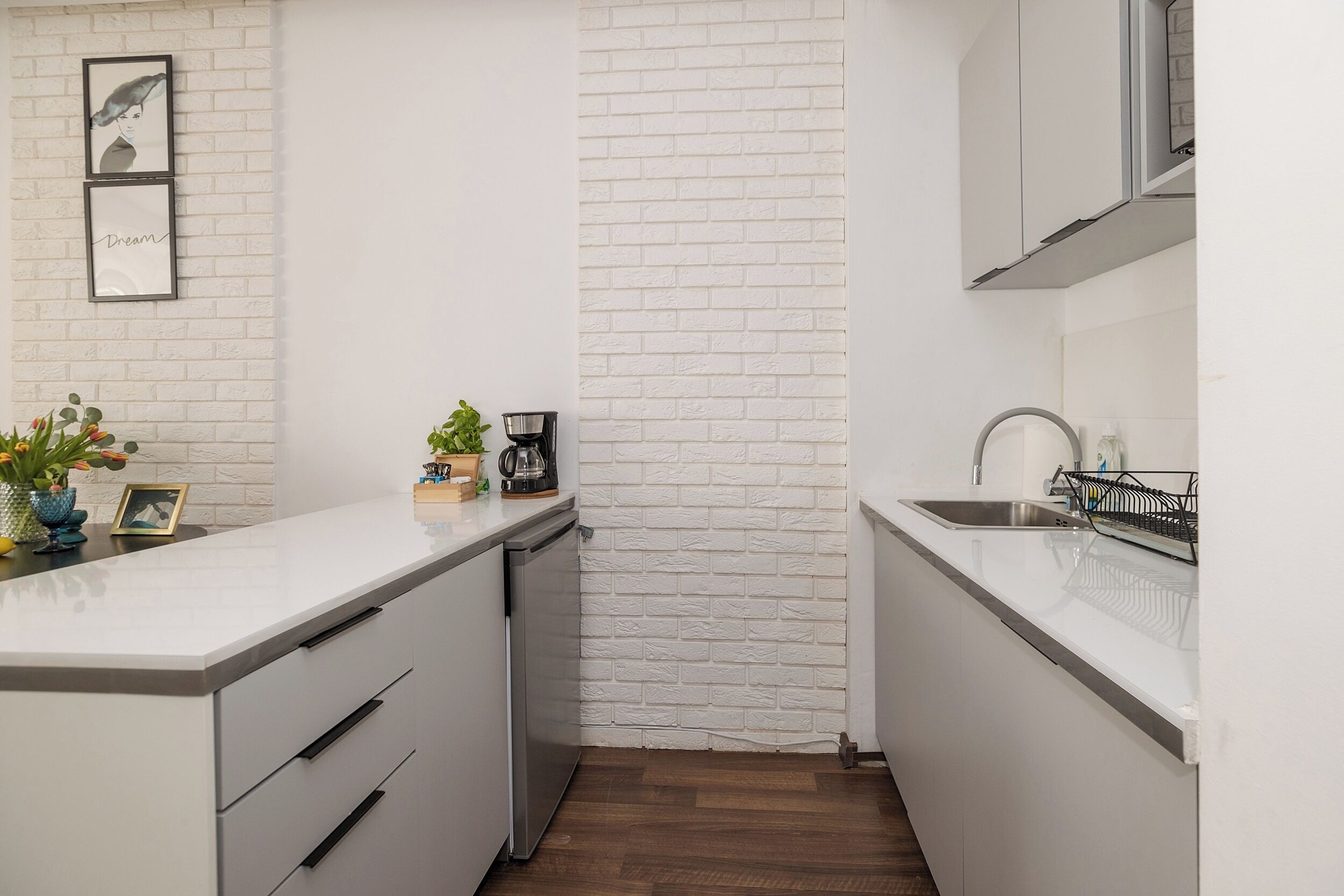 Una cocina moderna con armarios blancos, una pared de ladrillo decorativa y una pequeña encimera con una cafetera y plantas.