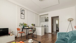 A modern living room with a sofa, a dining table with chairs, a kitchen area, and a TV on a stand. - ShortStayPoland Sielecka B183 (Warsaw)