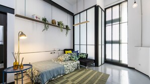A modern bedroom with a bed, bedside table, lamp, and a large window.