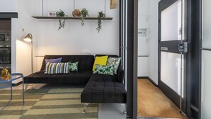 A modern living room with a sectional sofa, a small table, a lamp, and a shelf with plants.