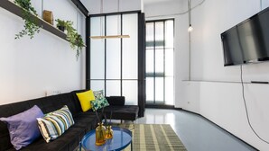 A modern living room with a black sofa, a blue coffee table, and a large TV on the wall.