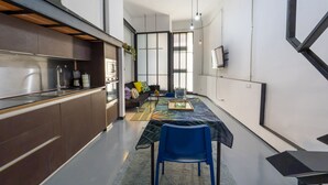 A modern kitchen with stainless steel appliances, a dining area with a table and chairs, and a sofa in the background.