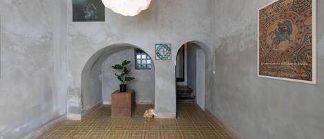 Un pasillo con piso estampado, dos pilares de madera, una planta en maceta y una obra de arte enmarcada en la pared.