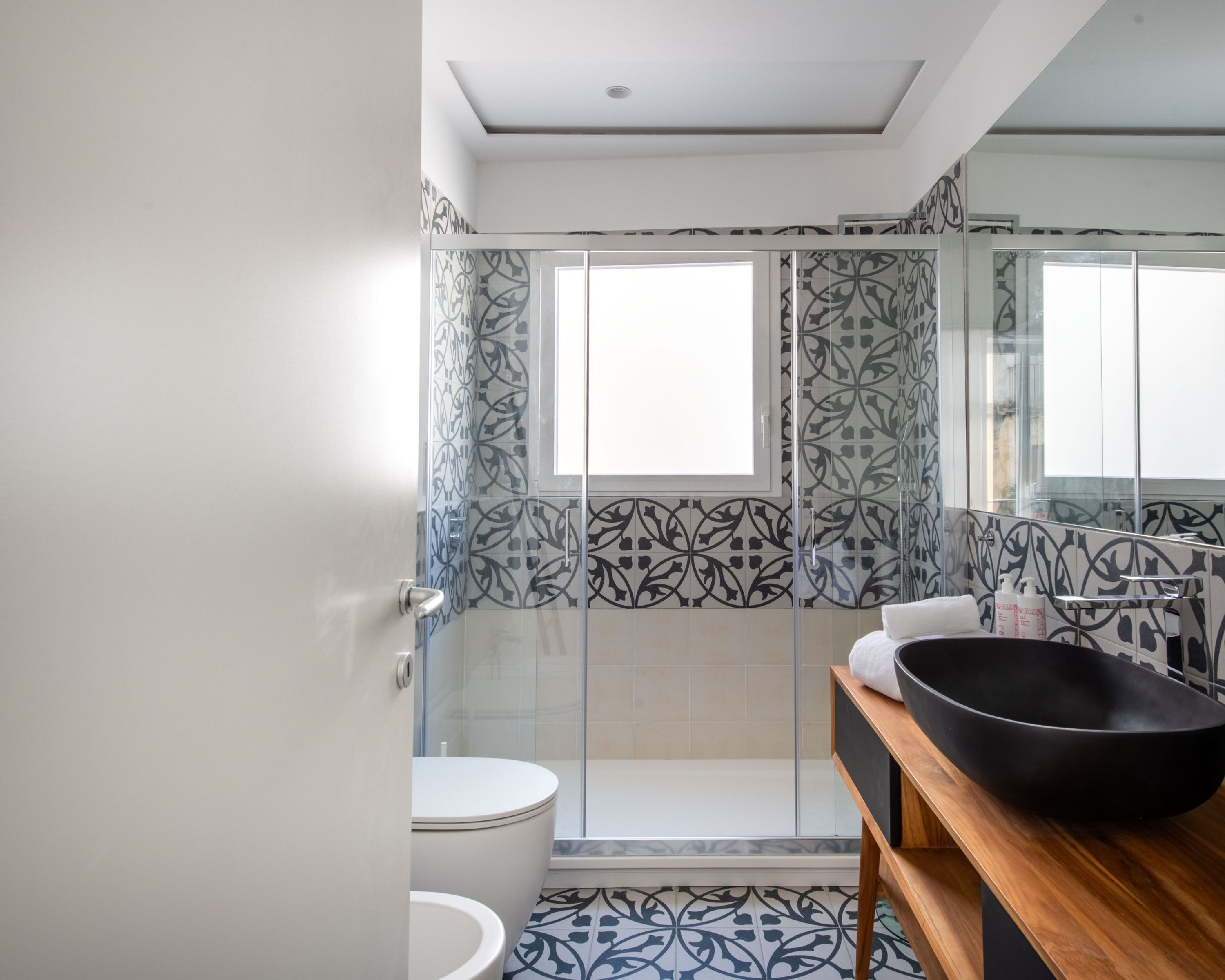 A modern bathroom with a glass shower enclosure, a white toilet, and a wooden vanity with a black basin.