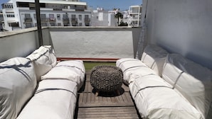 Une terrasse sur le toit dotée de sièges rembourrés blancs et d’un pouf en osier tressé.