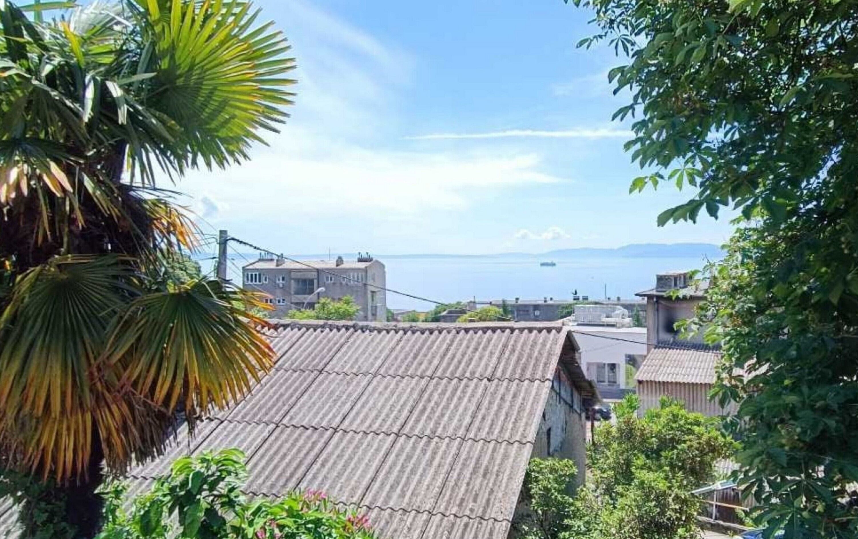 A coastal residential area with traditional buildings, a clear view of the sea, and lush greenery.
