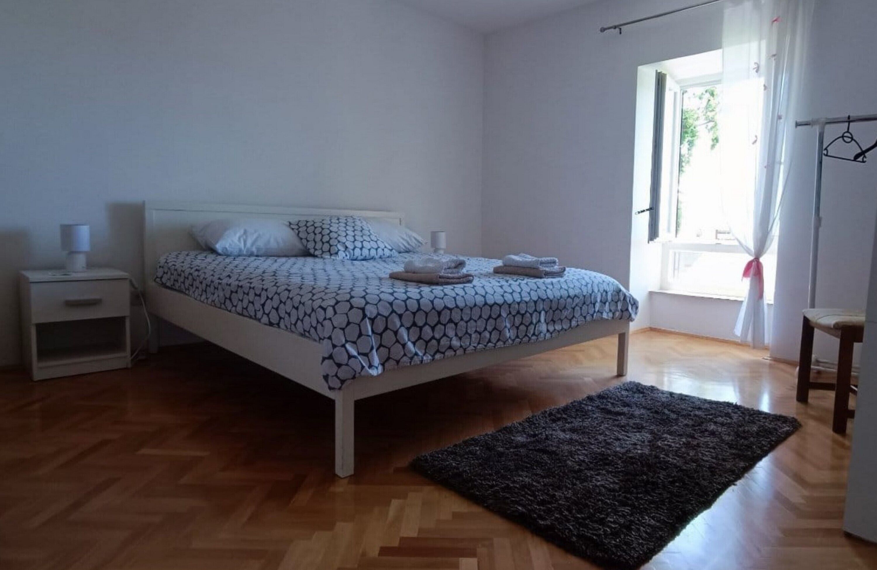 Une chambre à coucher comprenant un lit, une table de chevet, une petite table, une fenêtre avec des rideaux et une vue sur la verdure à l’extérieur.