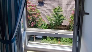 A window with a view of a corrugated metal roof, pink flowering plants, and a palm tree. - Luxury apartment Ivone with balcony (Rijeka)