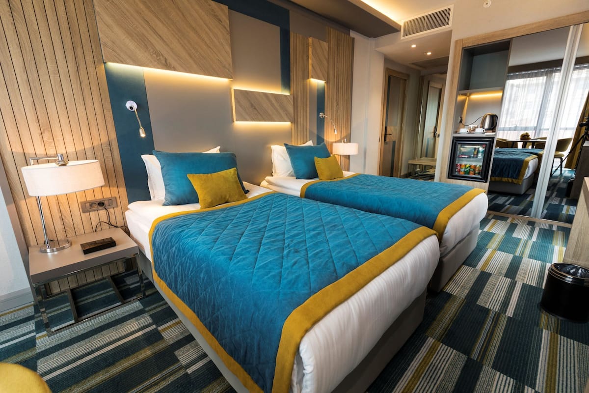 A hotel room with two beds, a nightstand, a desk, a refrigerator, and a bathroom visible through an open door.